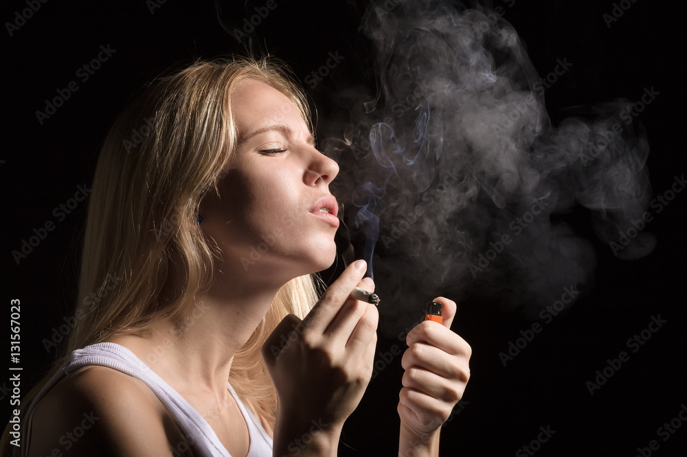 Obraz premium woman smoking joint of marijuana on black background