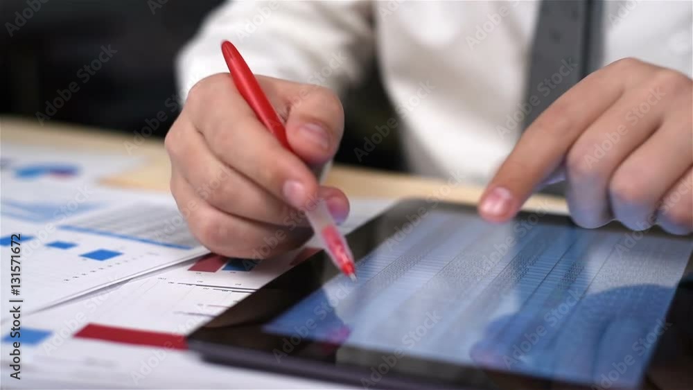 Businessman Compares Data On Tablet And Business Documents Businessman Compares Data On Tablet And Business Documents