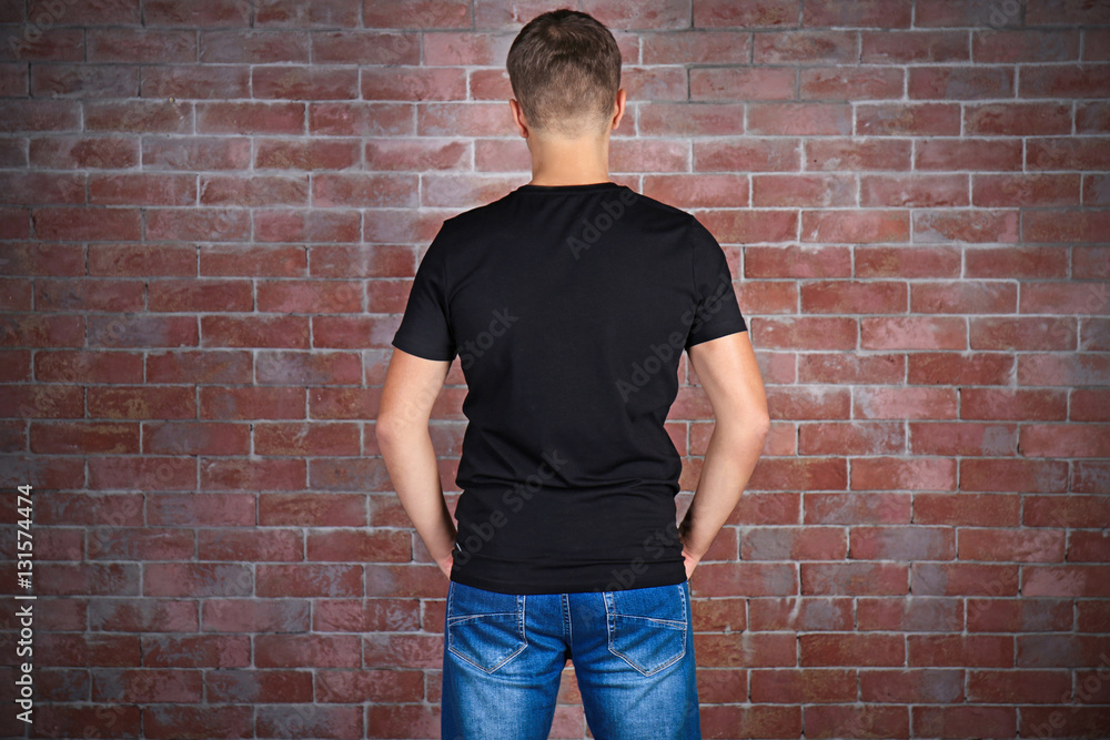 Handsome young man in blank black t-shirt standing against brick wall Handsome young man in blank black t-shirt standing against brick wall