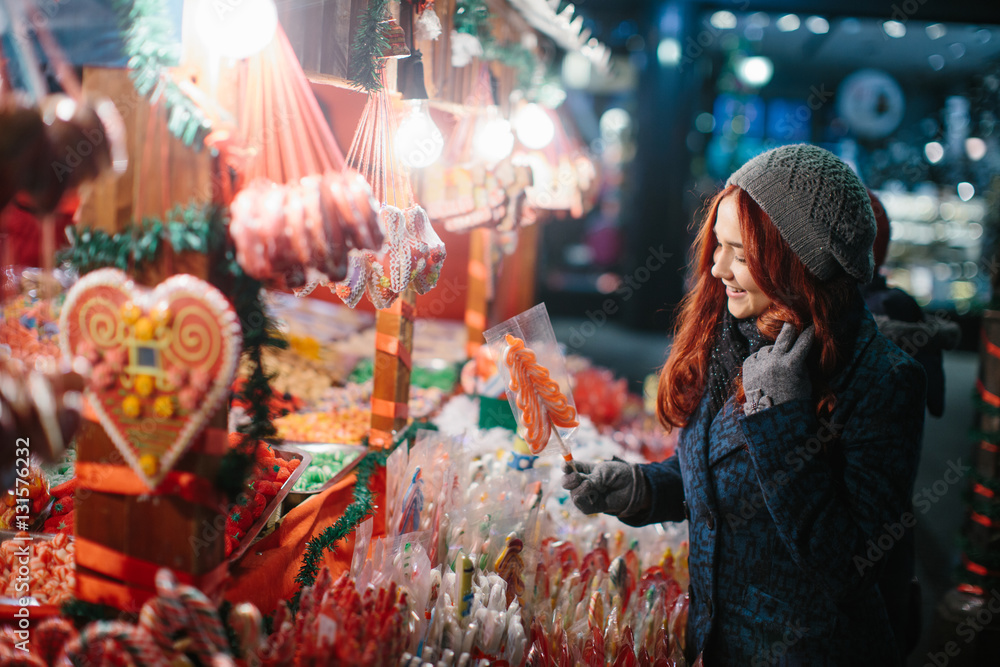 Beautiful young woman buying candy at Christmas market in evening time