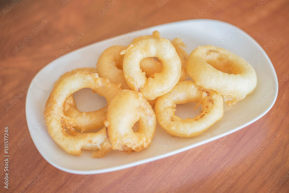 Fried onion rings in white dish on wooden background. Fast food.