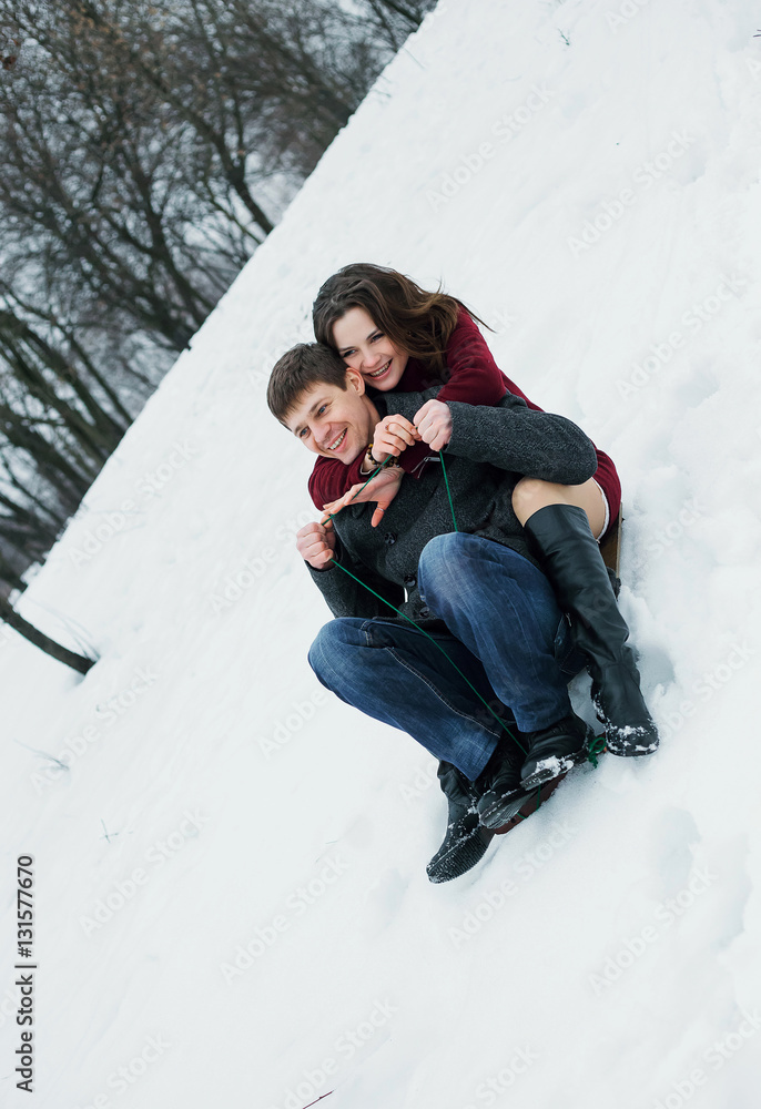 Funny man and a beautiful girl, they go from the mountain on a sled. Romantic feelings and positive emotions, joy. Scenic winter walk in Park. Fantastic shooting. Fashionable toning. Creative color.