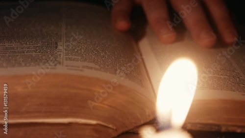 dolly shot of a man turning pages through an ancient book lit by candles