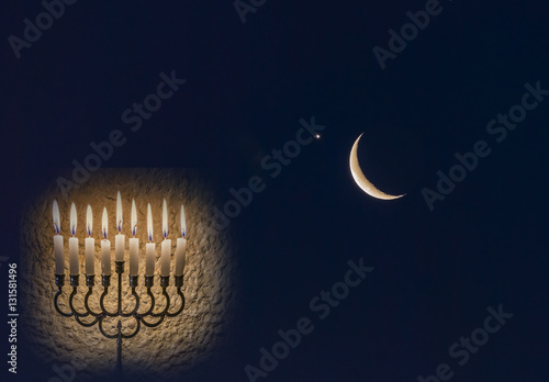 Low key composite image with menorah with glitter lights of burning candles and crescent moon on black nocturnal sky photo