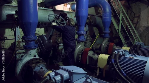 A woman twists the industrial valve on pumping station, she twirls it
