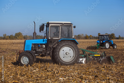 Two big blue tractor plowing a field and remove the remains of previously mown corn. The work of agricultural machinery. Harvest