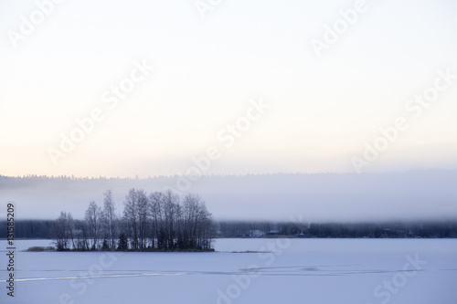 Foggy winter morning. Small island. Ice covered with snow. Foggy mountains in the background. © Jne Valokuvaus