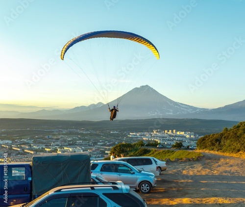 PETROPAVLOVSK-KAMCHATSKY, RUSSIA - 28 JULY, 2013: Paraglider flying over Petropavlovsk-Kamchatsky on the background of the cone of the volcano Karyaksky at sunset photo