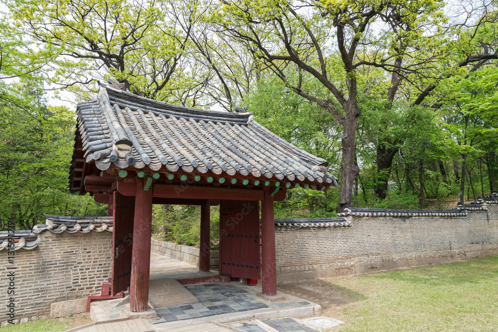 Verdant trees, wooden gate and stone wall next to the Jeongjeon - the main hall of the Jongmyo Shrine in Seoul, South Korea.