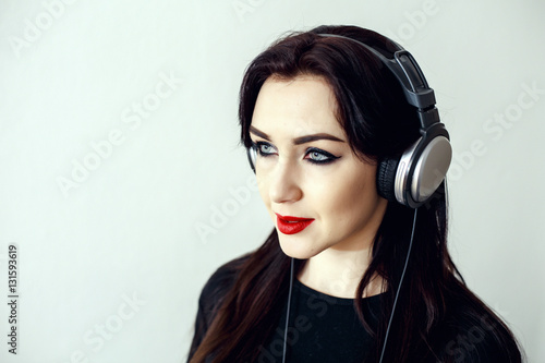 Happy pretty smiling woman with red lips in a black jacket listens to music in headphones over white background