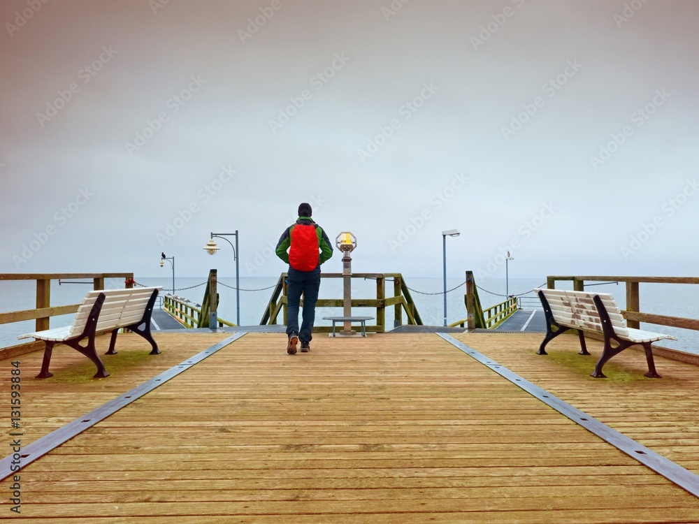 Tourist with red backpack on wooden sea pier. Man in trekking suit