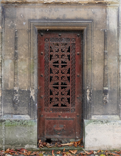 Fotografi Old and weathered red / brown closed iron door in a stone wall of an old tomb / crypt at a graveyard
