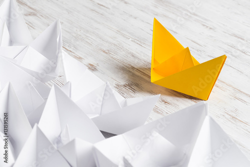 Business leadership concept with white and color paper boats on wooden table