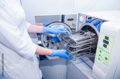 Dentist assistant's hands get out sterilizing medical instruments from autoclave. Selective focus