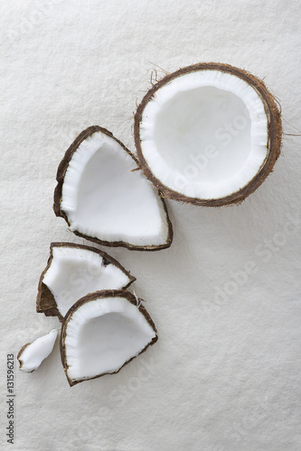Pieces of a whole coconut cracked open on a textured white background and viewed from above