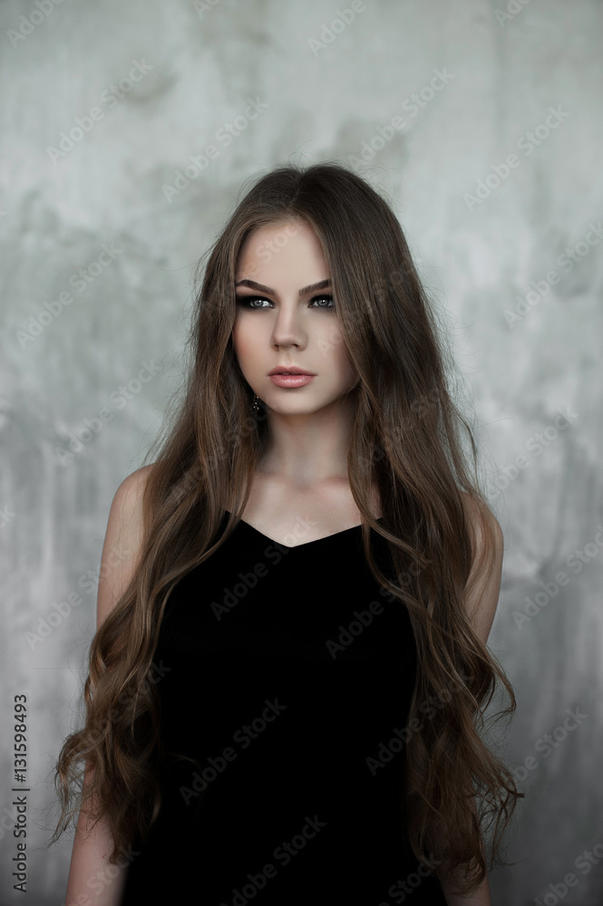 Fototapeta premium Young girl with long beautiful hair and smoky eyes wearing black maxi evening dress. Studio shot