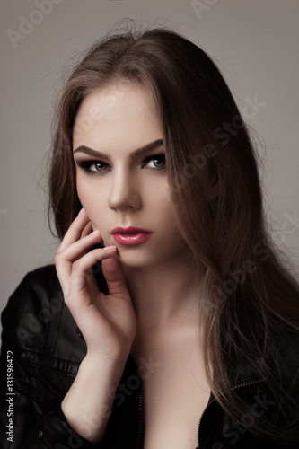 Young girl with long beautiful hair and smoky eyes wearing black leather jacket and jeans. Studio shot. Close up