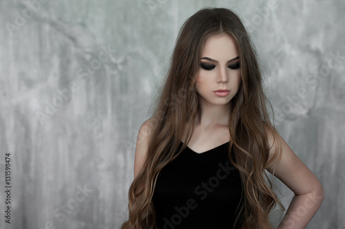 Young girl with long beautiful hair and smoky eyes wearing black maxi evening dress. Studio shot