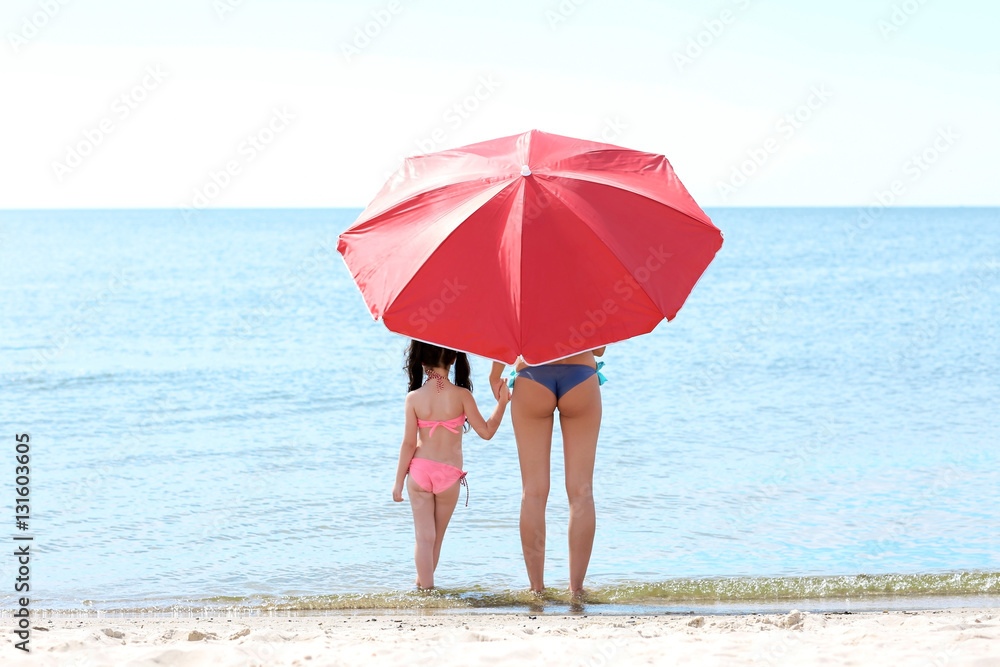 Mother and daughter with umbrella relaxing  on beach