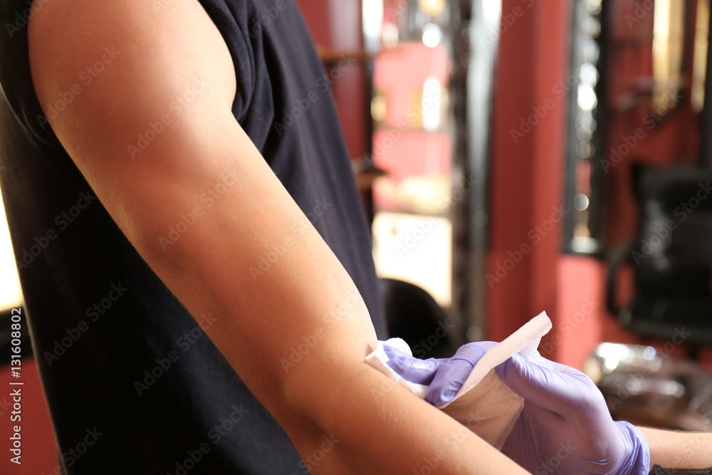 Fototapeta premium Tattoo master in studio applying antiseptic onto skin