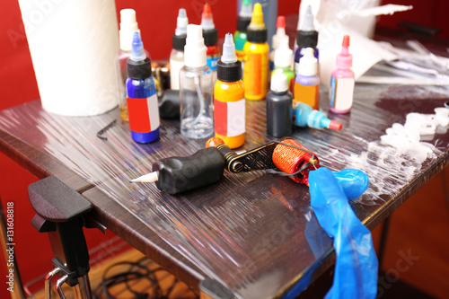 Tattoo machine and bottles with colorful inks on wooden table, close up view