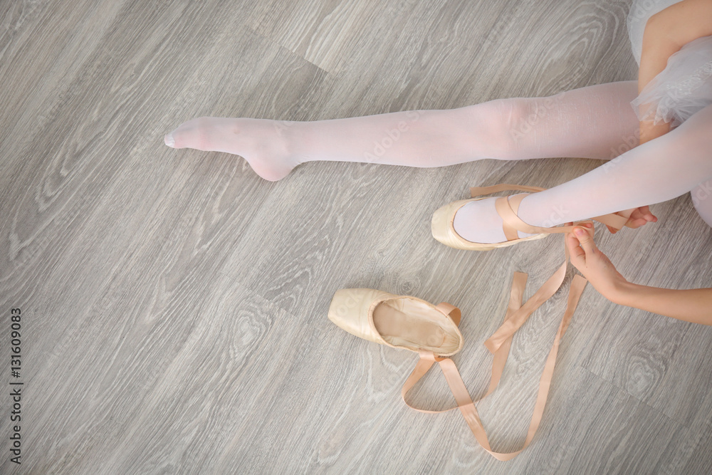 Fototapeta premium Ballerina tying ballet shoes on wooden floor