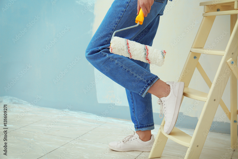 Young female decorator with paint roller in room, closeup