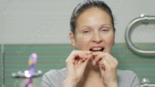 Young attractive woman using dental floss in the bathroom of the hotel room. She carefully chitit holes between the teeth and check the result at the end photo