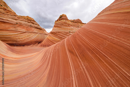 Colorful and swirling sandstone waves, under a stormy and cloudy sky, at The Wave - a dramatic erosional sandstone rock formation located in North Coyote Buttes area at Arizona-Utah border.