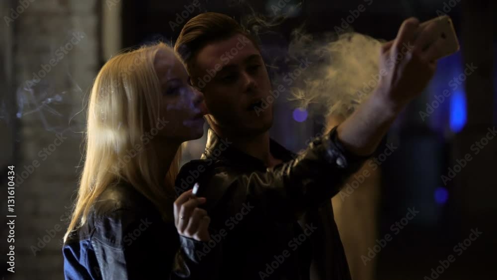 Young man and woman smoking and making selfie on smartphone at nightclub Young man and woman smoking and making selfie on smartphone at nightclub