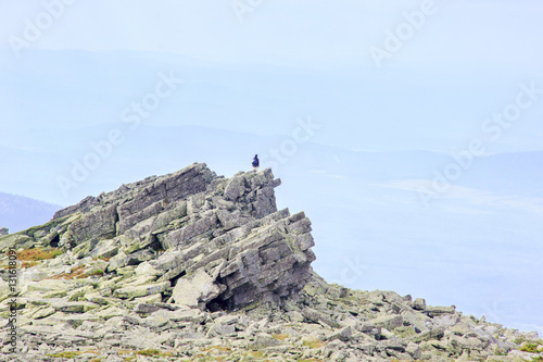 Man silhouette with backpack stay on sharp rock peak, watching down to landscape.