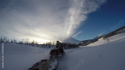 Wallpaper Mural Snowmobile pulled sled on snow-covered road in forest on background active Klyuchevskoy Volcano erupting ash, steam, gas at sunset. Kamchatka Peninsula, Russia, Klyuchevskaya Group of Volcanoes. Torontodigital.ca