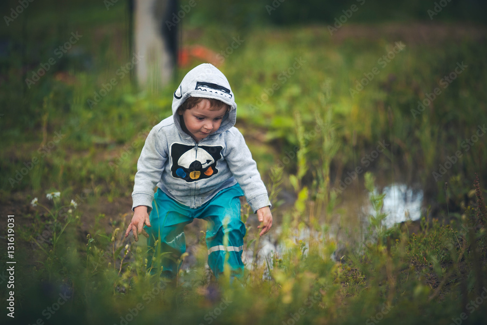 Cute curly baby dressed in boots and rubber pants jumping in a puddle. Funny kid with children's happiness. Cute curly baby dressed in boots and rubber pants jumping in a puddle. Funny kid with children's happiness.