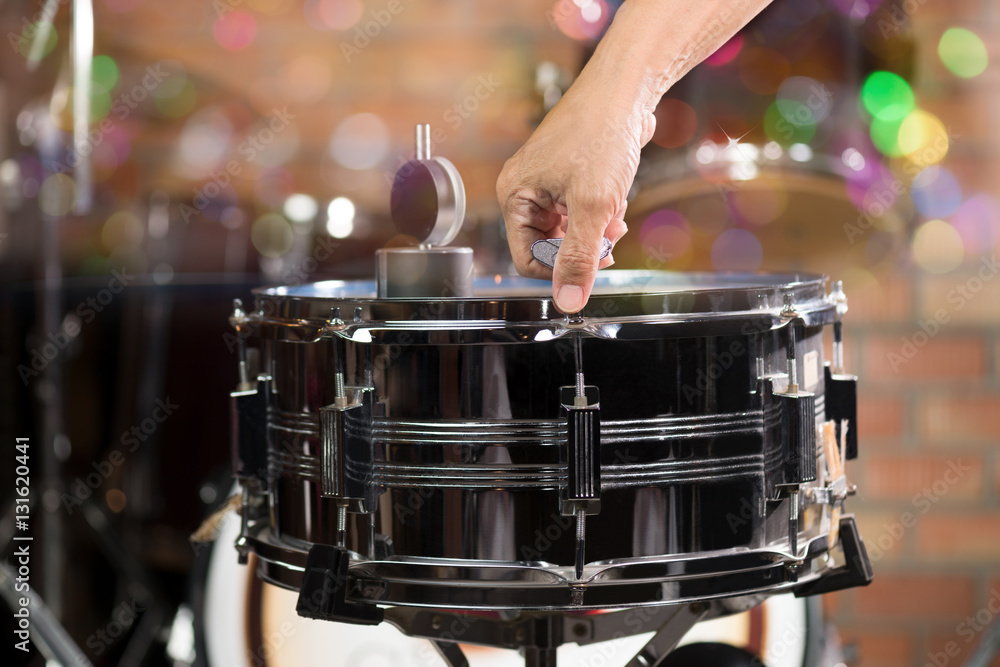 Hand adjusting tension rod of snare drum.Drummer measuring batter
