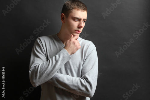 Thoughtful young man posing in a gray sweater on a black background.