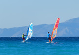 Back view of two windsurfers in action mooving parallel to each other