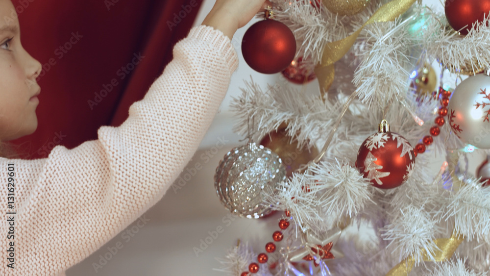 Naklejka premium Girl hangs Christmas balls at christmas tree