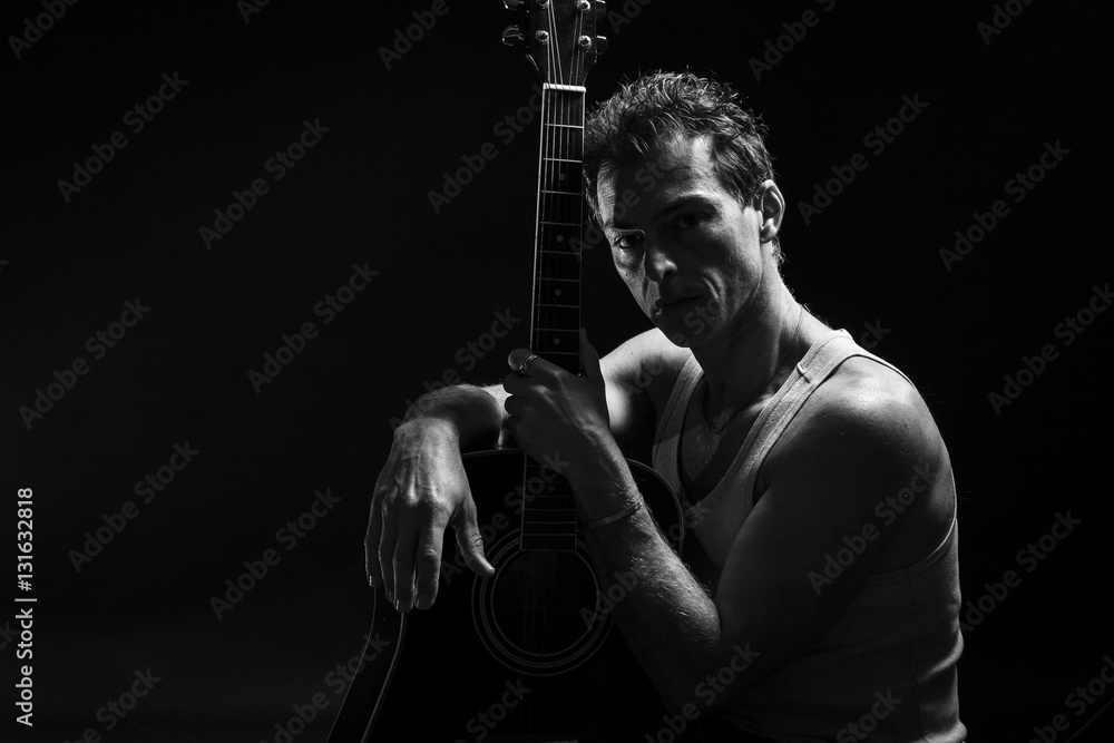 Low key portrait of man with his guitar. Dark background