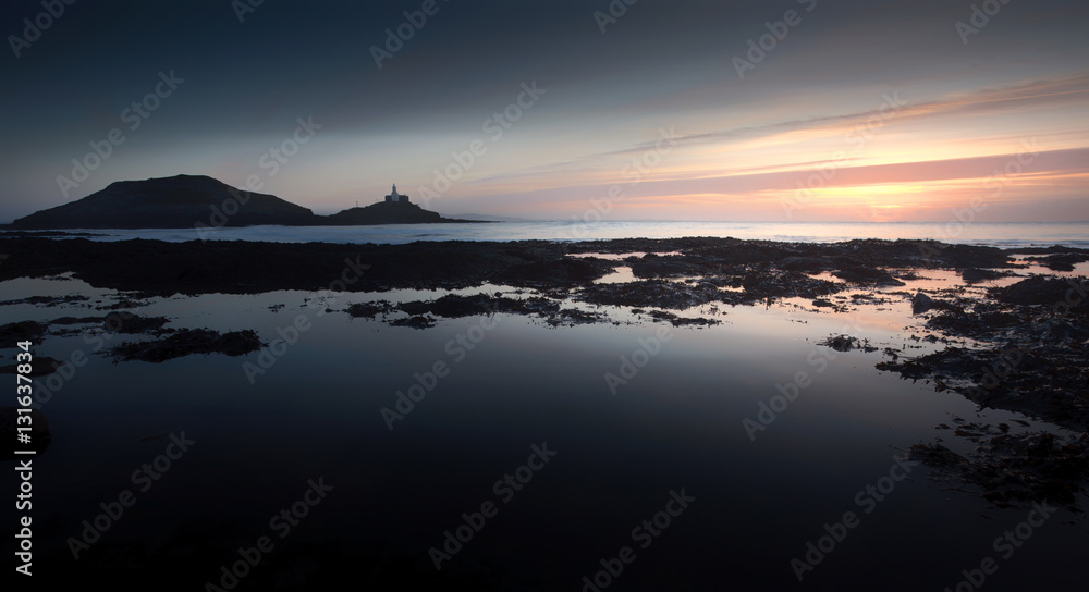 Early morning, big rockpools and Mumbles Lighthouse on a low tide at Bracelet Bay on the Gower peninsula in Swansea, UK
