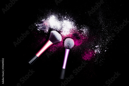 Makeup brushes with powder spilled glitter dust on black background. Pink powder on black table.
