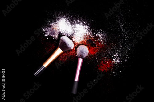 Makeup brushes with powder spilled glitter dust on black background. Red powder on black table.