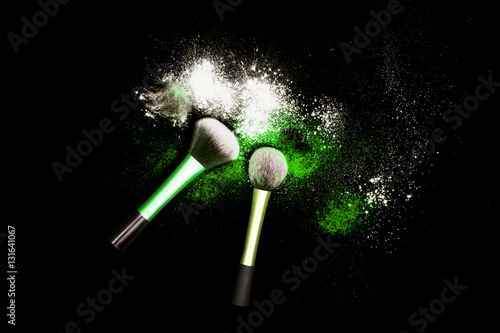 Makeup brushes with powder spilled glitter dust on black background. Green powder on black table.