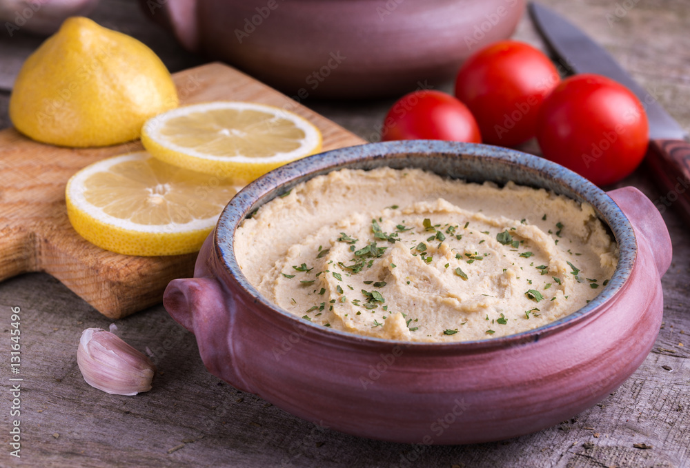 Humus in homemade bowl with lemon and tomatoes on natural wooden desk. Humus in homemade bowl with lemon and tomatoes on natural wooden desk.