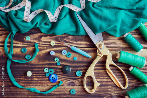sewing tools, green fabric, threads and buttons on a wooden background