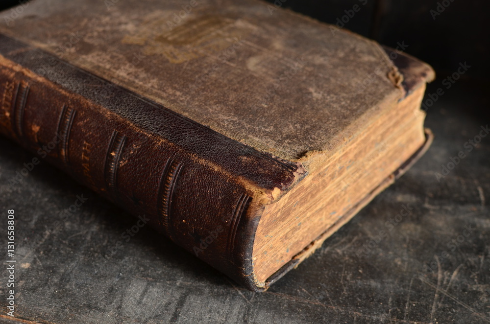 Obraz premium Old leather bound book laying on a dusty wooden bookshelf