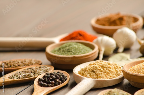 Different spices in bowls and wooden spoons on the table