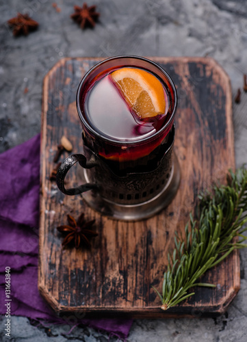 Mulled wine with orange and spices in vintage glass cup holder on wooden board. Concrete background. Hot drink. Top view.