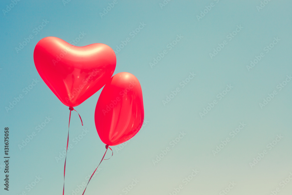 Two red heart shaped balloons in flight