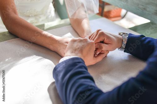 Bride and groom sitting at the table  holding hands. © sergo321