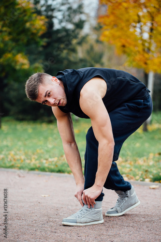 Fitness man tie shoelaces in the fall park.